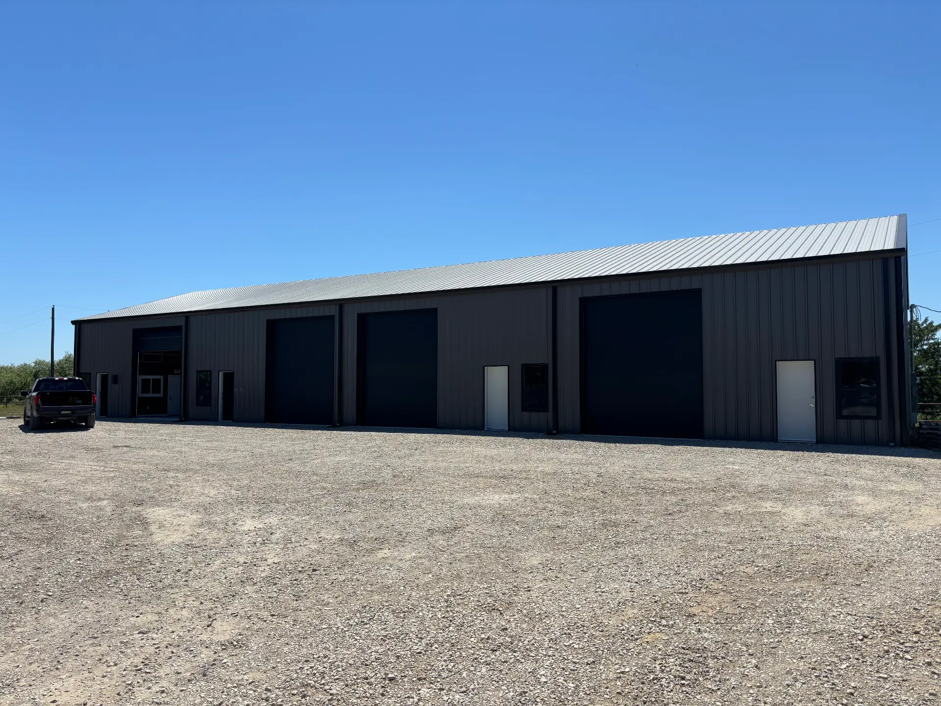 Dark grey metal flex building with black roll-up doors on a crushed concrete lot